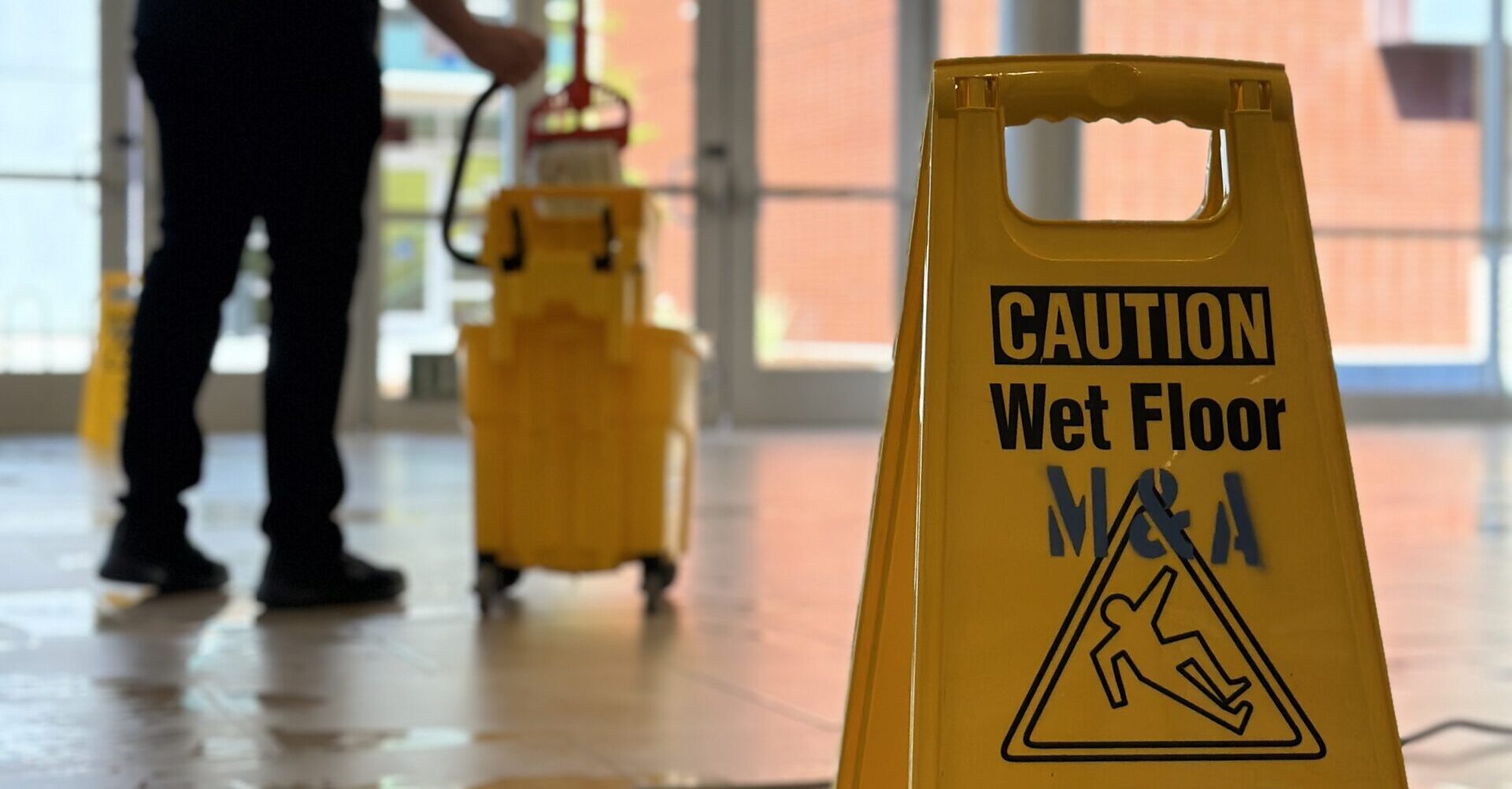 caution wet floor sign in the foreground with a person mopping in the background