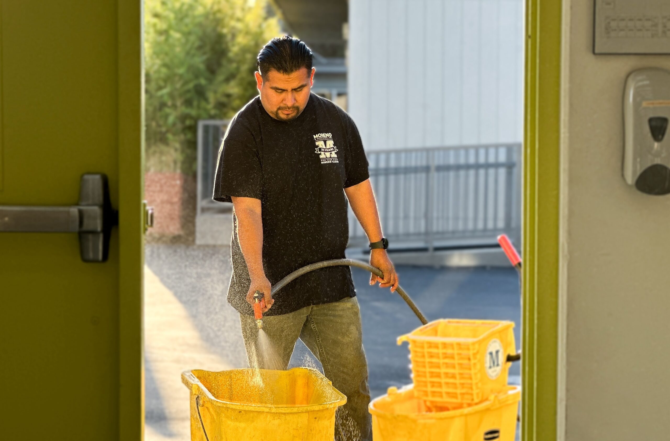 man in doorway filling up two janitorial buckets with a water hose.